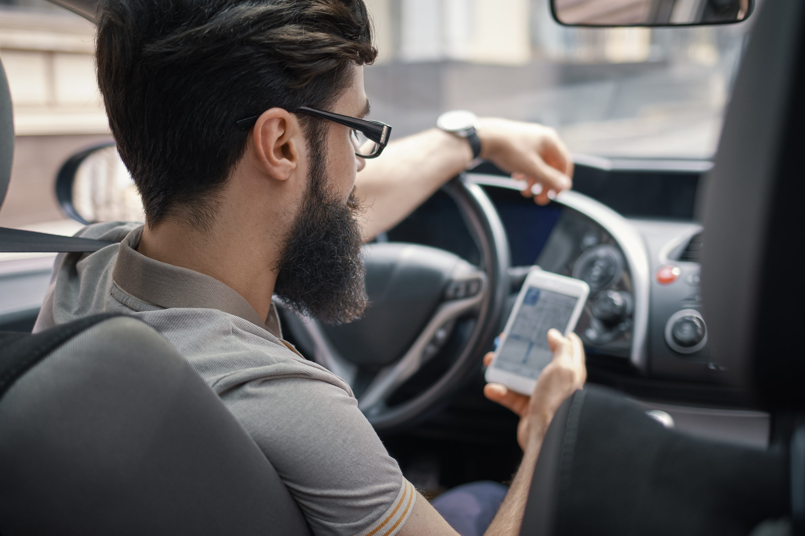 homem de barba e óculos usando o celular dentro do carro para ver a nova cnh brasileira