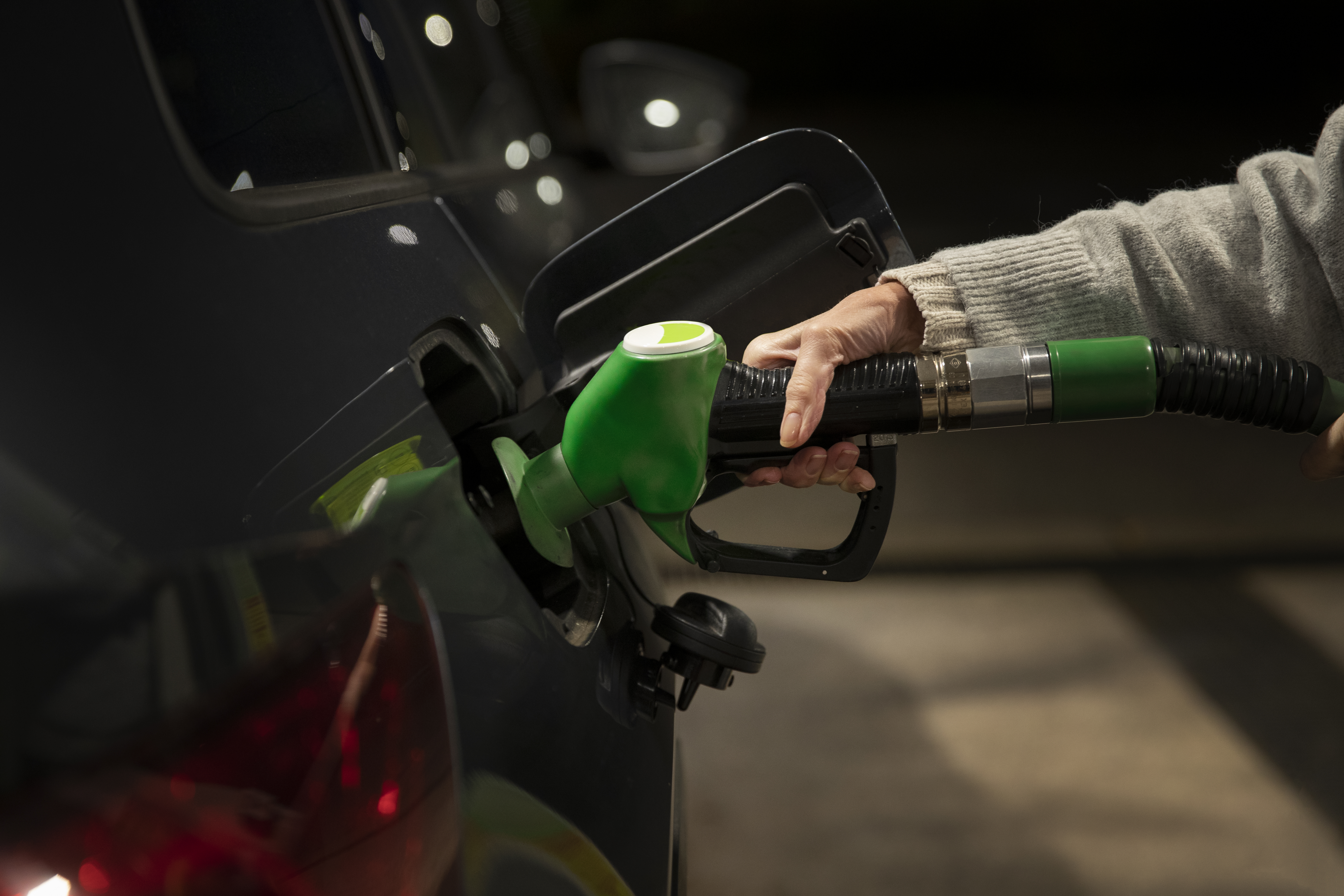 Mão de uma pessoa segurando uma bomba de gasolina e abastecendo um carro
