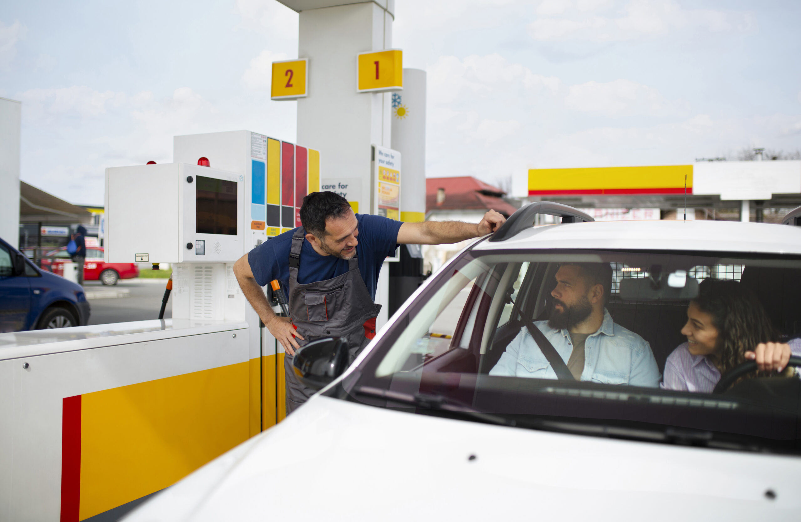 Frentista em posto de gasolina atendendo outro homem dentro de um carro branco