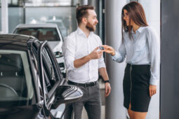 Homem branco recebendo a chave do seu novo carro de uma mulher branca na loja