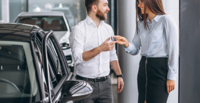 Homem branco recebendo a chave do seu novo carro de uma mulher branca na loja
