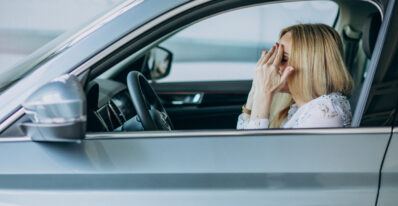 Mulher loira dentro de um carro cinza com as mãos na cabeça, frustrada