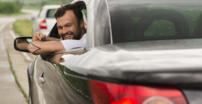 Homem branco feliz acenando para trás pela janela do seu carro